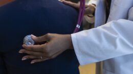 Photo of a physician in white coat listening to patient's lungs with a stethascope